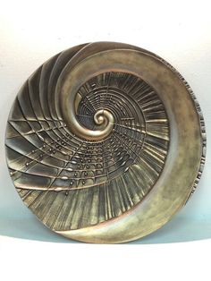 a metal plate with spiral design on the bottom and sides, against a white wall