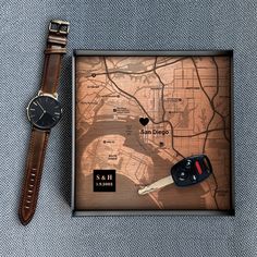 a watch is sitting next to a wooden map with a car key on it and a leather strap