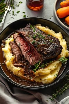 a steak and mashed potatoes in a skillet with carrots on the side