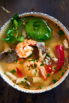 a bowl of soup with shrimp, peppers and green garnish on the side