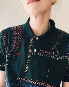 a woman wearing a green shirt with colorful stitching on the front and sides, looking to her left