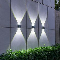 three lights are lit up on the side of a concrete wall in front of some bushes