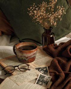 a cup of coffee sitting on top of an open book next to a vase with flowers