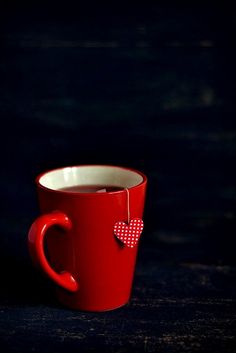 a red coffee cup with a heart decoration on the handle and inside sitting on a table