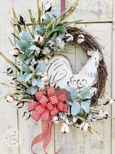 a heart shaped wreath with cotton and greenery hanging on a door handle, decorated with a red gingham bow