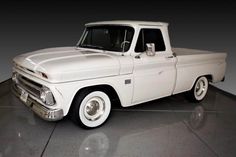 an old white pickup truck is parked in a room with black walls and flooring