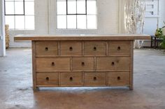 an old wooden dresser sitting in front of two windows with white brick walls and flooring