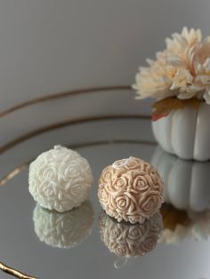 two decorative white balls sitting on top of a glass table next to a vase with flowers