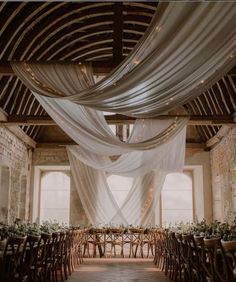 an indoor wedding venue with white draping and wooden chairs