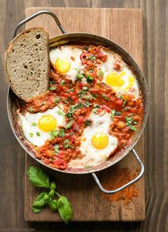 two eggs are in a skillet with tomato sauce and bread next to it on a wooden table