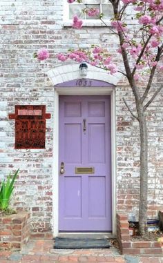 a purple door is in front of a brick building with pink flowers on the tree