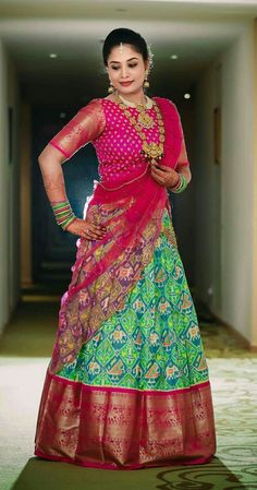 a woman in a green and pink lehenga standing on a carpeted hallway