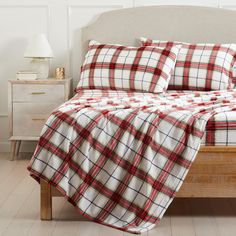 a bed with red and white plaid comforter on it's side, next to a night stand