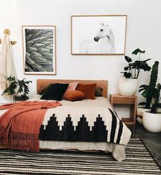 a bed sitting in a bedroom next to potted plants and pictures on the wall