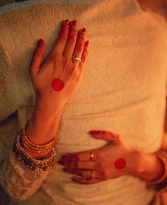 a woman with red painted hands on her belly and wearing gold bracelets, sitting in bed