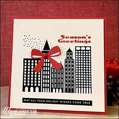 a christmas card with a red bow on the front and black buildings in the back that says season's greetings