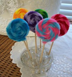 four colorful lollipops in a glass vase on a table