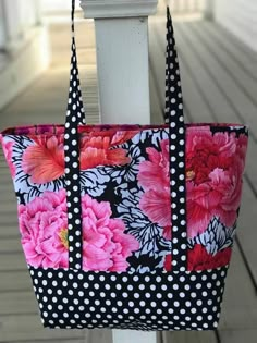 a black and white polka dot bag with pink flowers on the front is hanging from a pole