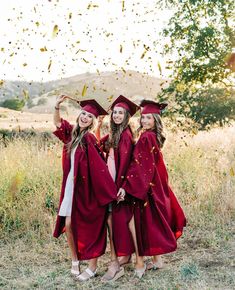 three girls in red graduation gowns are throwing confetti