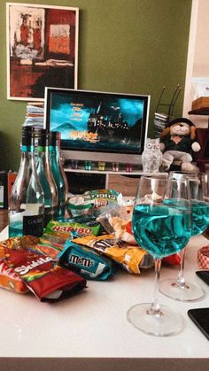 two wine glasses sitting on top of a white counter next to snacks and drinks in front of a computer monitor