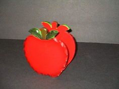 a red apple shaped vase sitting on top of a black table next to a gray wall