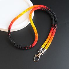 an orange, yellow and black beaded lanyard on a white plate next to a pair of scissors