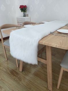 a dining room table with a white fur runner on it's long wooden legs