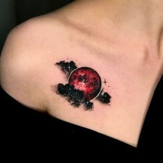 a woman's shoulder with a red and black tattoo on her left shoulder, in the shape of a planet