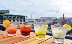 three different colored drinks sitting on top of a wooden table next to each other with buildings in the background