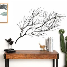 a wooden table topped with books next to a cactus and a wall mounted art piece