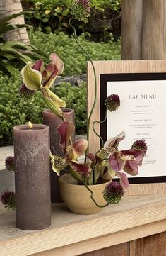 an arrangement of flowers and candles sit on a table with a menu in the background