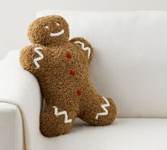 a brown teddy bear sitting on top of a white couch next to a pillow that is shaped like a gingerbread man