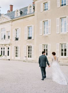 a bride and groom holding hands walking in front of a large building with white windows