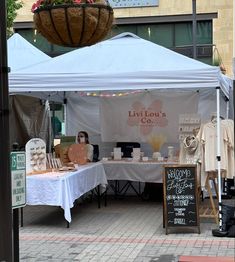 an outdoor market with tables and chairs under a white tent that says livi lou's co