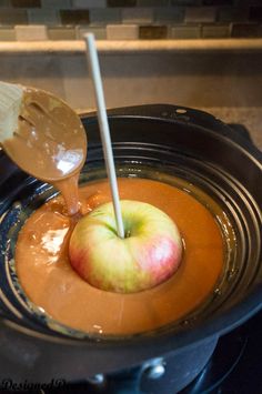 an apple is being dipped in caramel sauce with a spoon on the stove top