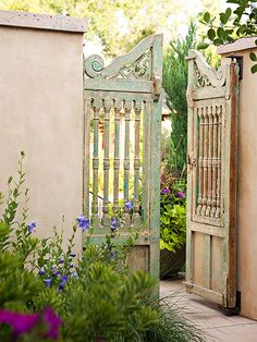 an open gate in the middle of a garden with purple flowers and greenery around it