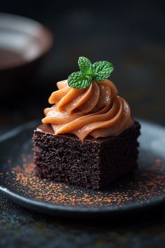 a piece of chocolate cake with frosting and a leaf on top is sitting on a black plate