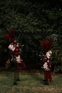 two tall black vases with red and white flowers on them in front of trees