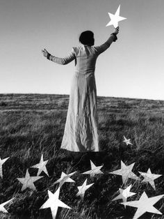 a woman standing on top of a grass covered field with stars in the air above her