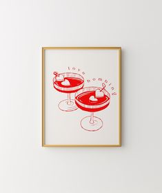 two red glasses with drinks in them on a white wall next to a gold frame