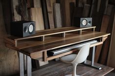 a computer desk with speakers and a keyboard on it's stand in front of a wooden wall