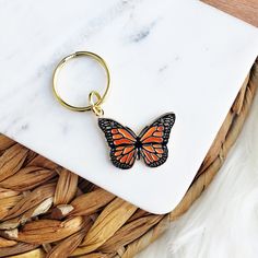 an orange butterfly keychain sitting on top of a white marble counter next to feathers