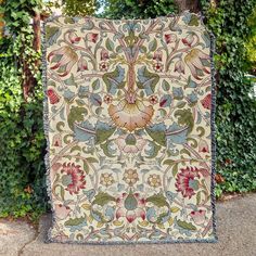 an intricately designed tapestry hanging on the side of a tree in front of some bushes