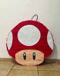 a red mushroom shaped purse sitting on top of a tile floor next to a wall