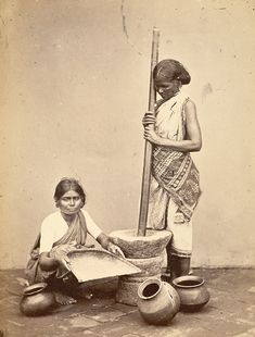 two women are sitting on the ground with pots and a pole in front of them