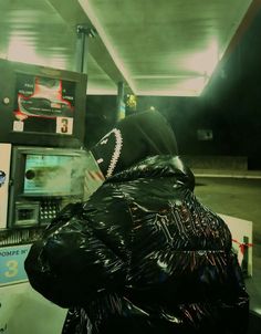 a man in a black jacket is at a gas station with his head covered by plastic