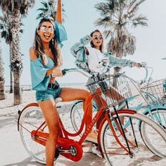 two women riding bikes on the beach with palm trees