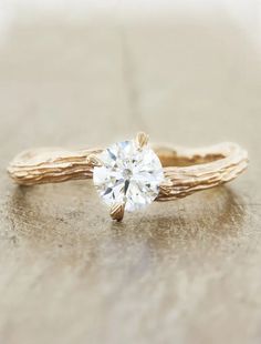 a gold ring with a white diamond in it sitting on a wooden table next to a piece of driftwood