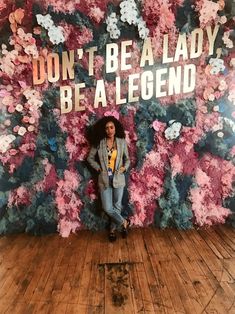 a woman standing in front of a floral wall with the words don't be a lady, be a legend