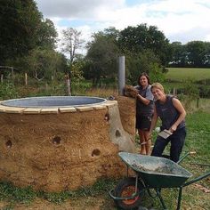 two people standing in front of a large round structure made out of hay and wood